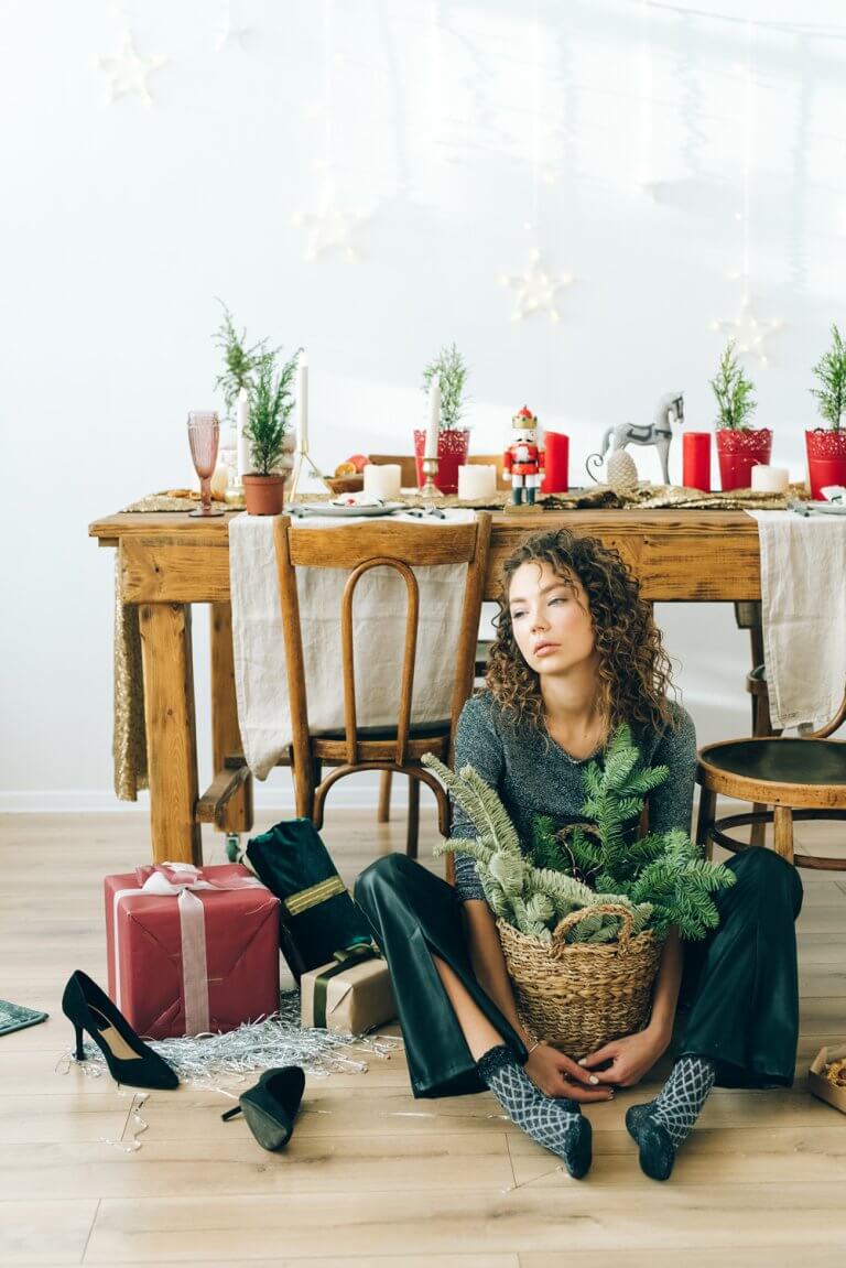 Woman sitting on floor surrounded by holiday decorations | Holiday stress management